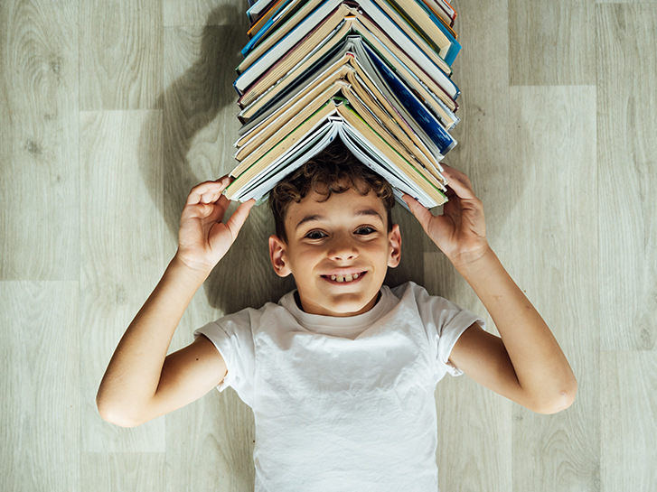 Einstiegsbild Oetinger Lektüren: Junge mit vielen Büchern auf dem Kopf