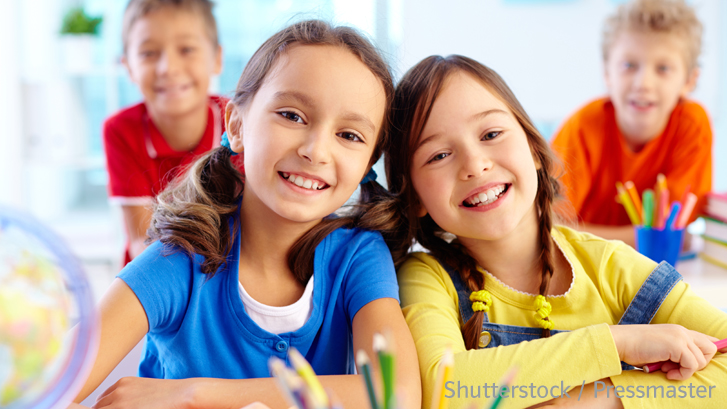 Zwei Schülerinnen und zwei Schüler im Hintergrund lächeln in die Kamera in einem Klassenzimmer
