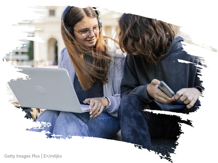 zwei Jugendliche schauen auf einen Laptop und freuen sich
