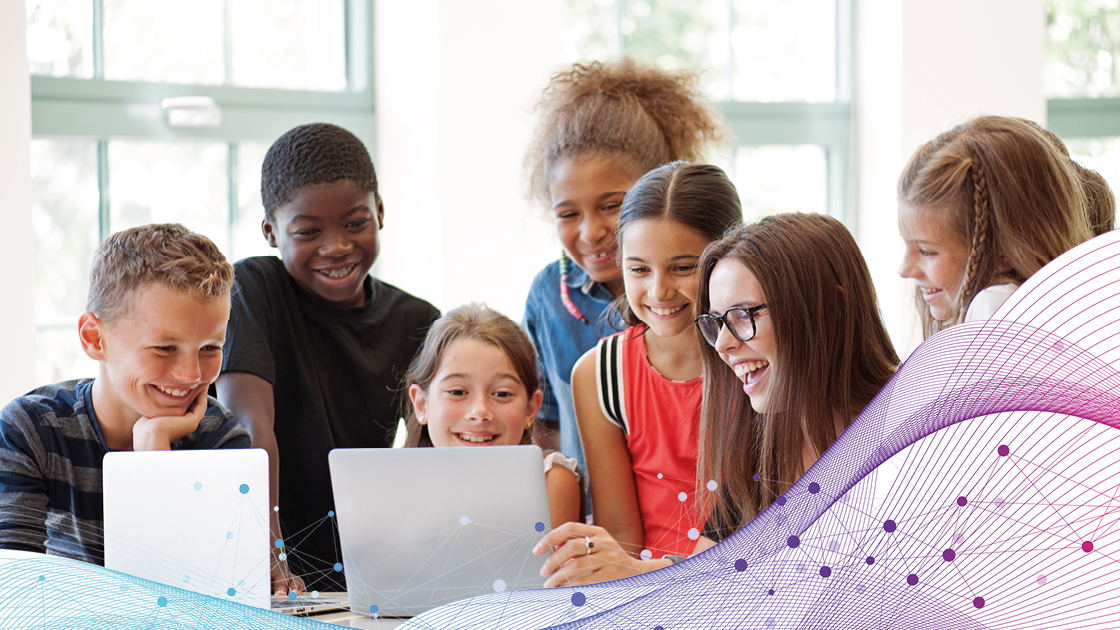 Kinder verschiedener Nationen schauen gemeinsam auf zwei Computerbildschirme im Klassenzimmer