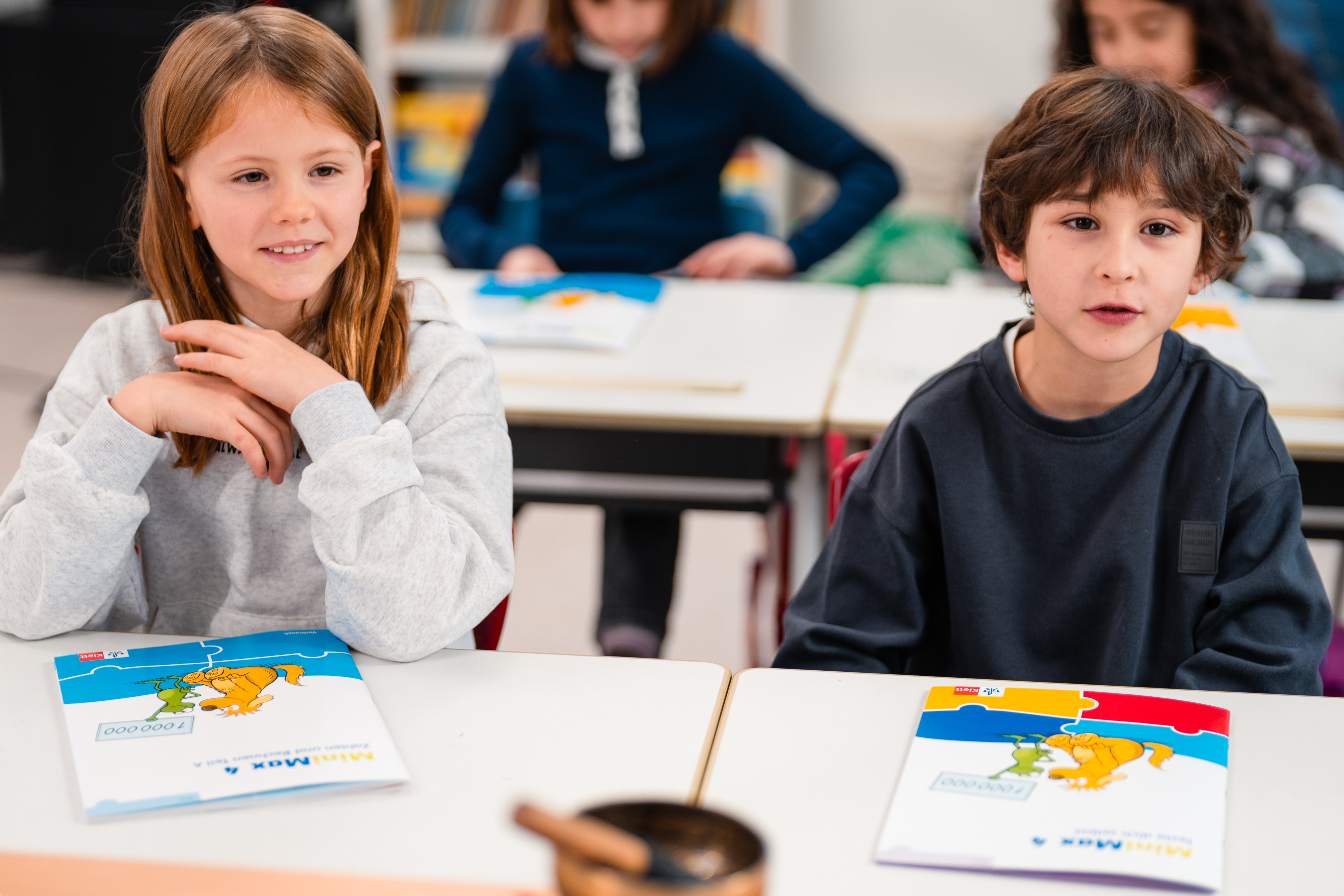 Zwei Lernende sitzen in einem Klassenzimmer an Tischen mit Lernmaterialien von „MiniMax 4“