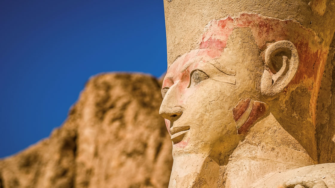 Eine altägyptische Statue mit detaillierten Gesichtszügen und einem Kopfschmuck vor einem klaren blauen Himmel Eine altägyptische Statue mit detaillierten Gesichtszügen und einem Kopfschmuck vor einem klaren blauen Himmel
