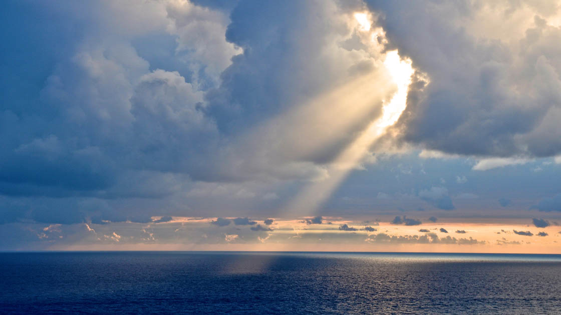 Eine Meereslandschaft bei Sonnenuntergang mit Wolken und durchbrechenden Sonnenstrahlen Eine Meereslandschaft bei Sonnenuntergang mit Wolken und durchbrechenden Sonnenstrahlen
