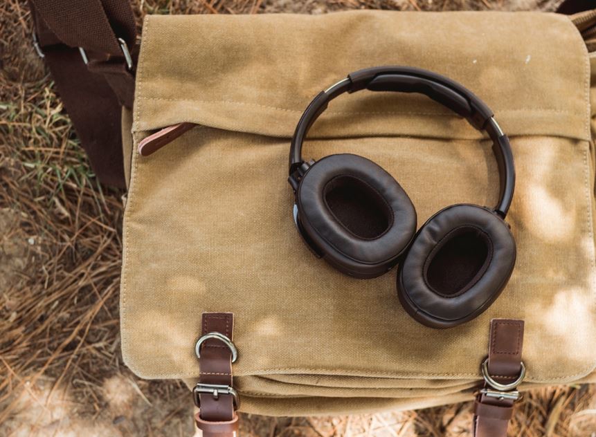 Schwarze Over-Ear-Kopfhörer liegen auf einer hellbraunen Leinentasche mit Lederriemen
