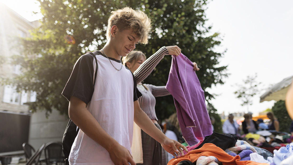 zwei Jugendliche schauen auf dem Flohmarkt Kleidungsstücke an zwei Jugendliche schauen auf dem Flohmarkt Kleidungsstücke an