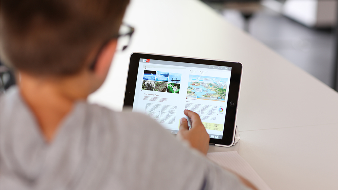 Ein Schüler blättert an einem Tablet in einem interaktiven eBook mit verschiedenen Bildern und Texten