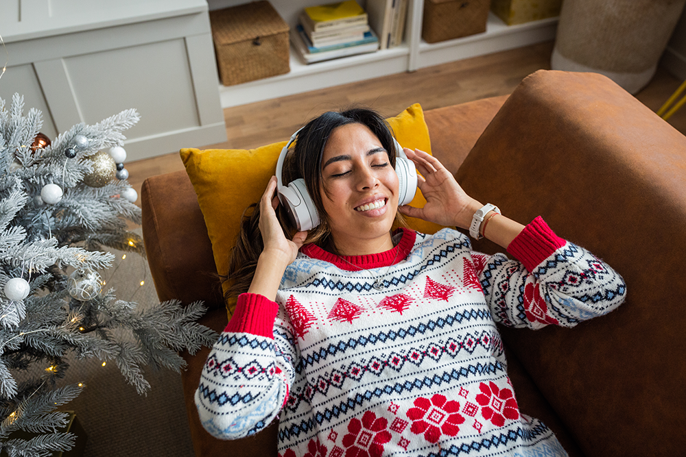 Frau im Weihnachtspullover hört mit Kopfhörern Musik