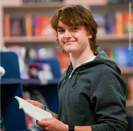 Junge mit Buch in der Hand lächelt in Kamera