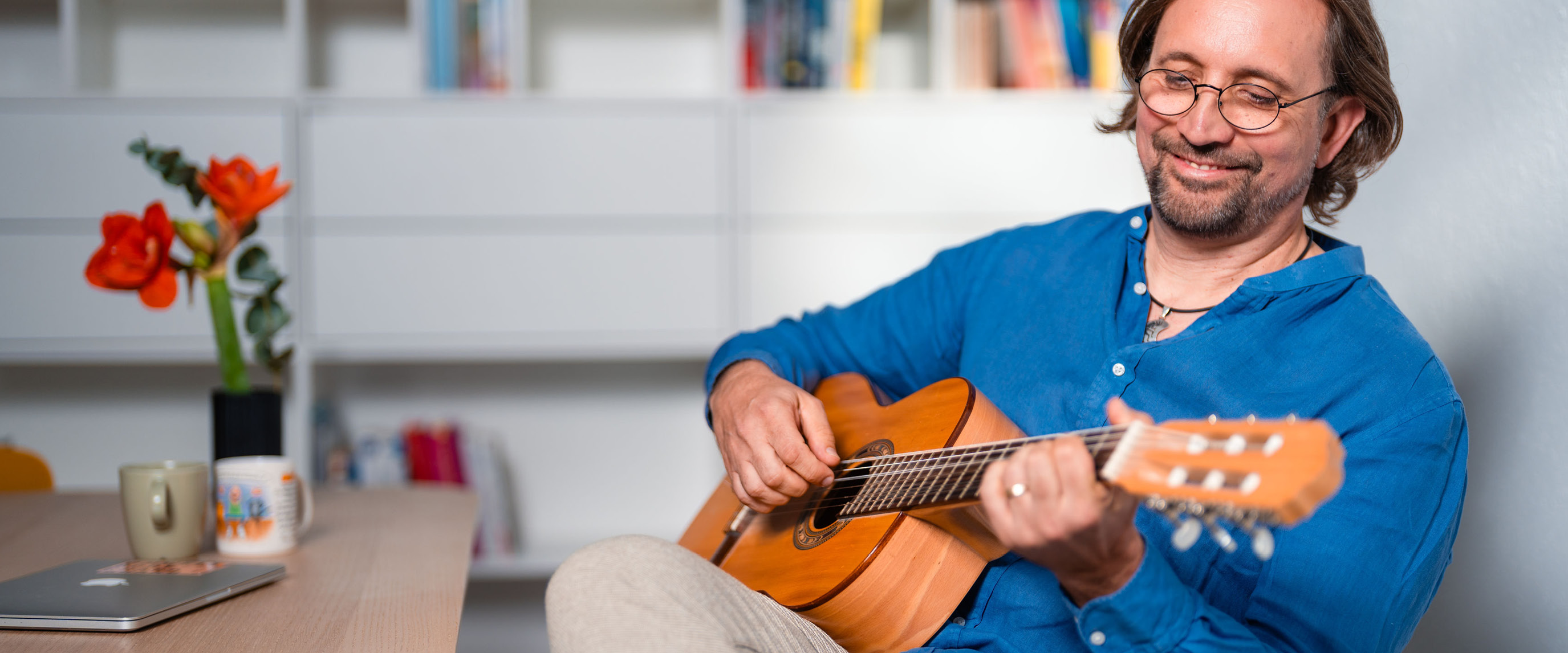 Lehrer sitzt mit Gitarre am Tisch und blickt auf das Instrument