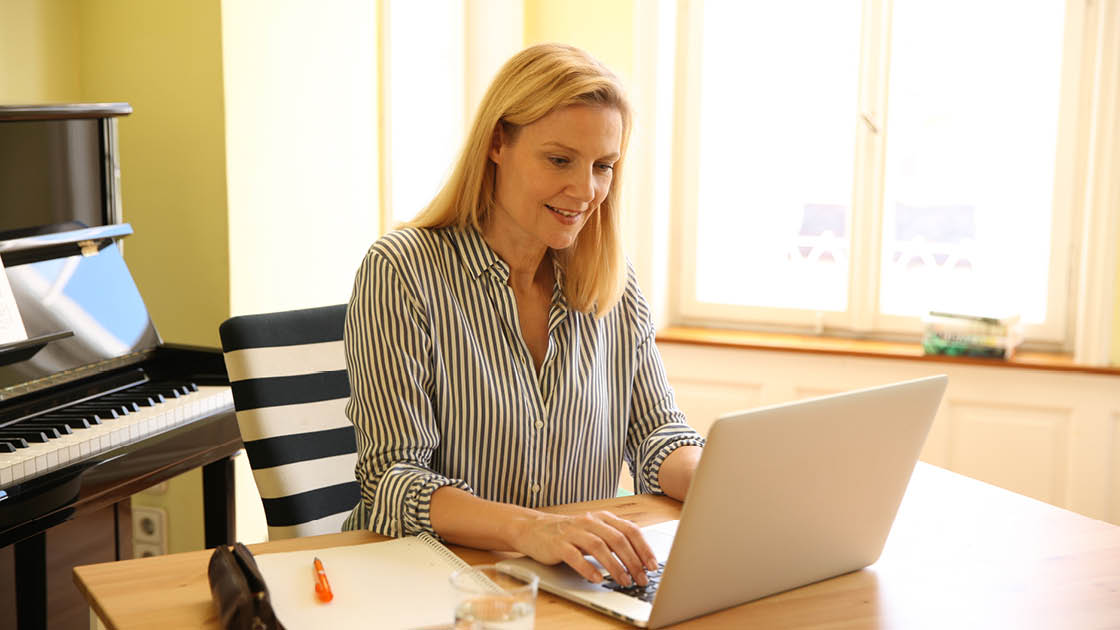 Eine Frau sitzt an einem Schreibtisch vor einem Laptop und lächelt