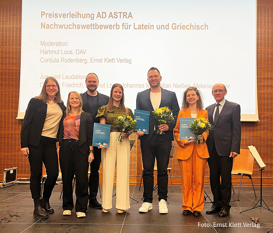 Mehrere Preisträger und Preisträgerinnen mit Urkunden und Blumensträußen vor einer Wand mit einer Präsentationsleinwand