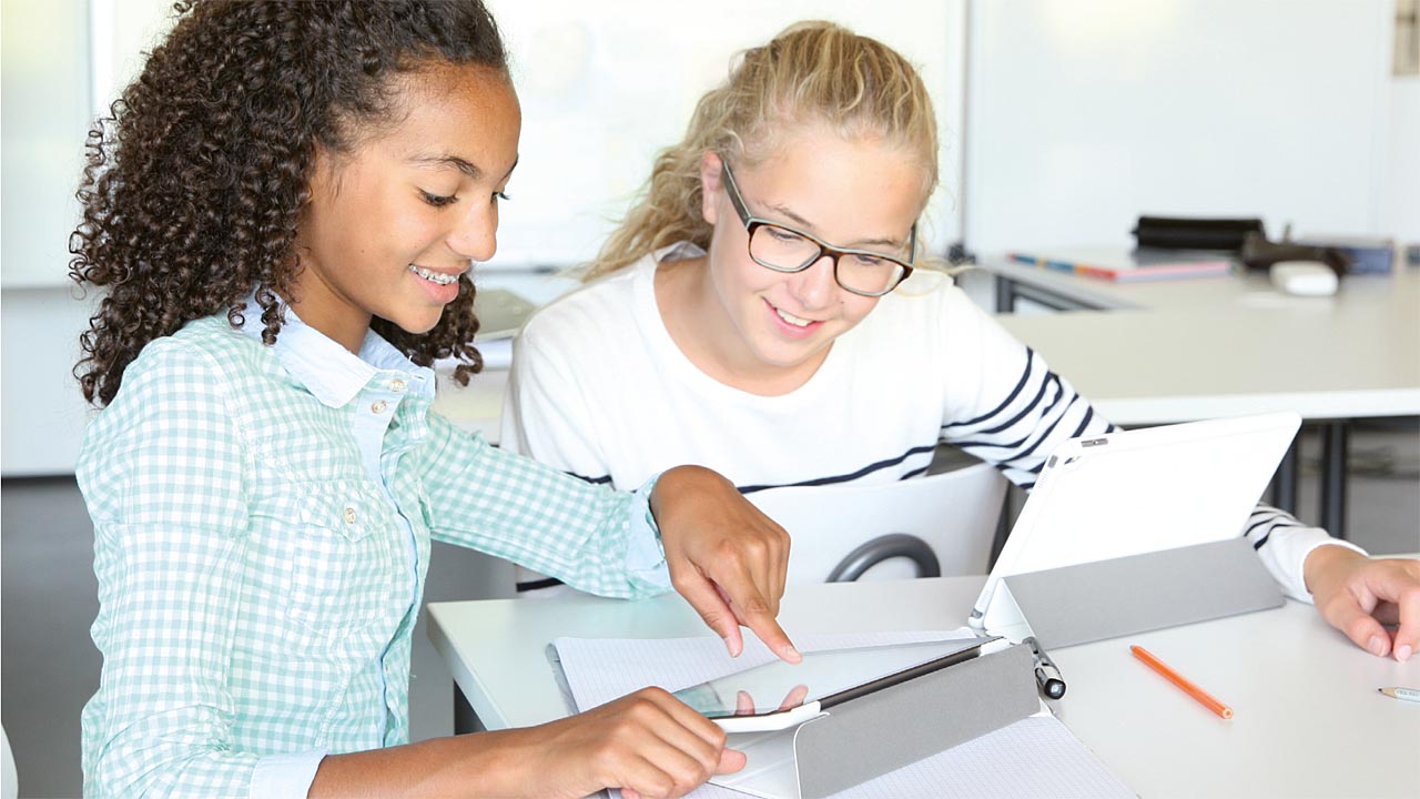 Zwei Schülerinnen sitzen in einem Klassenzimmer und nutzen Tablets