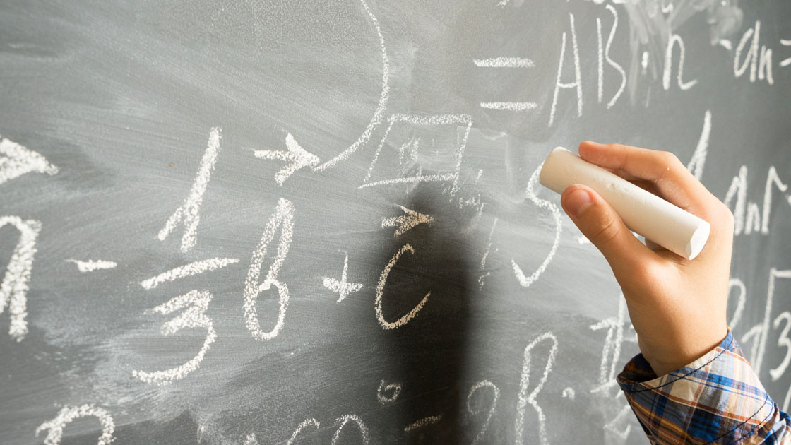 Eine Hand hält ein Stück Kreide und schreibt mathematische Gleichungen auf eine Tafel Eine Hand hält ein Stück Kreide und schreibt mathematische Gleichungen auf eine Tafel