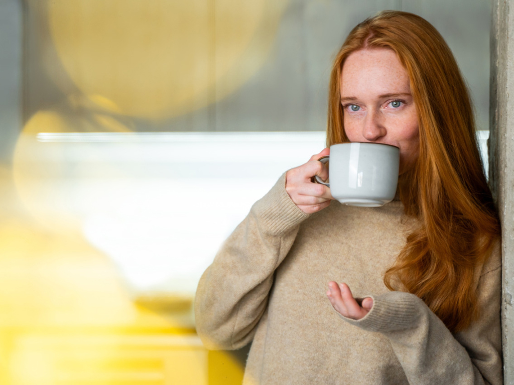 Porträt einer entspannten jungen Frau, die mit einer Kaffeetasse an der Wand lehnt