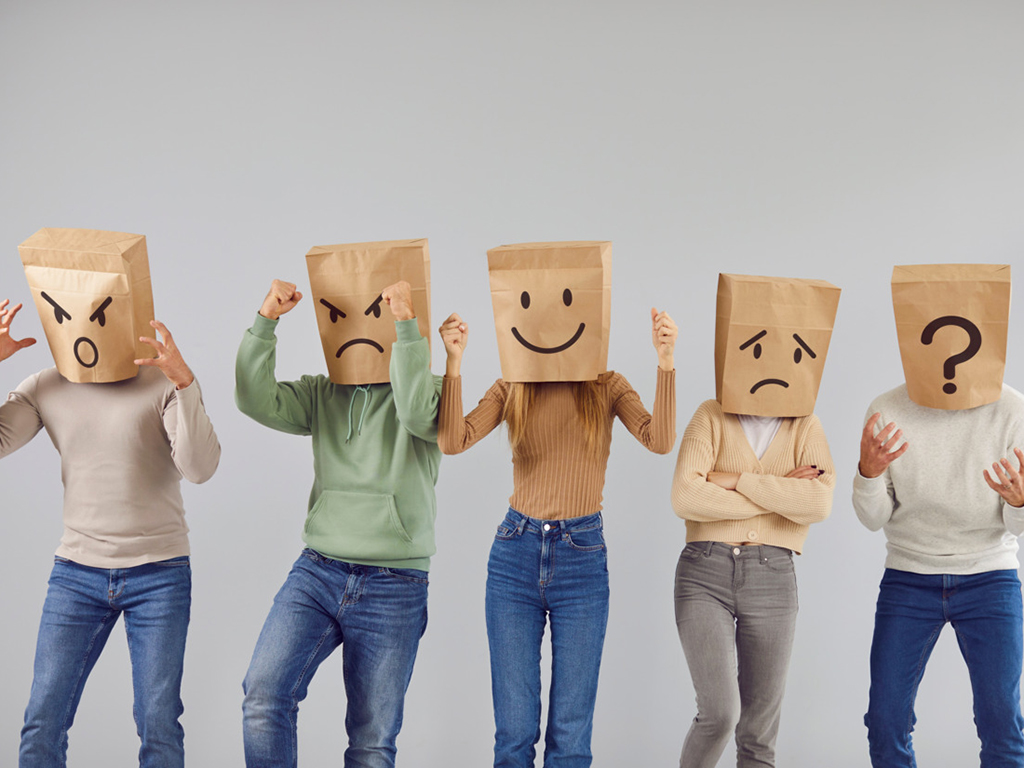 Verkleidete Personen tragen Papiertüten auf den Köpfen, die eine Vielzahl von Emotionen zeigen