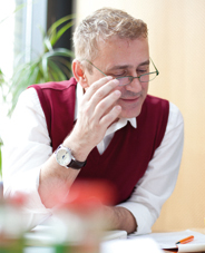 Ein Mann mit Brille, Hemd und Weste sitzt an einem Tisch und lächelt